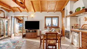 Amplia sala de estar con techo de madera, televisor, mesa de comedor con sillas y zona de cocina con estufa y armarios.