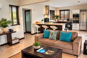 A modern living room with a sofa, coffee table, and a kitchen area in the background. - Seafront 1 bedroom large penthouse apartment on the beach at Pointe Aux Biches. (Trou-Aux Biches)