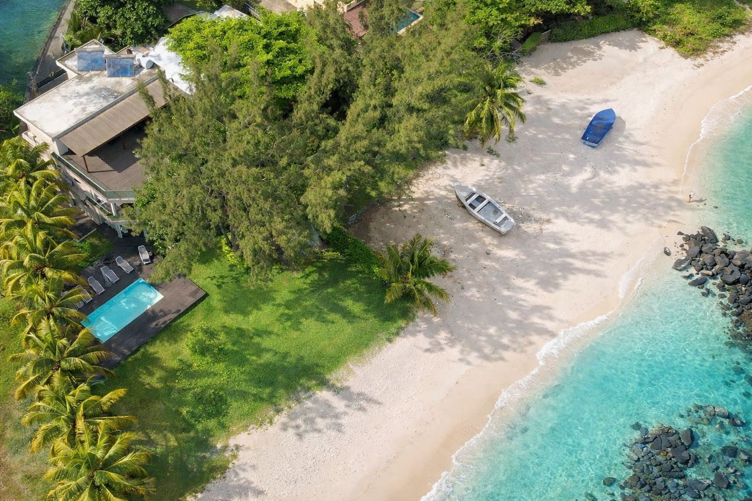 An aerial view of a beachside property with a swimming pool, lounge chairs, and a boat.