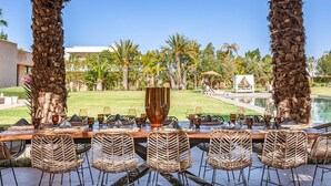 Un bar con sillas de mimbre, una piscina y vistas a un jardín con palmeras.