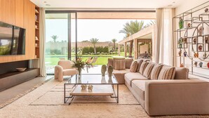 Una sala de estar moderna con sofá, mesa de centro, televisor y vista a un jardín.