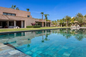A modern pool area with clear water, a lounge chair, and a building with large windows. - Villa Massinissa with pool - My Rental Homes (El Rhechat)