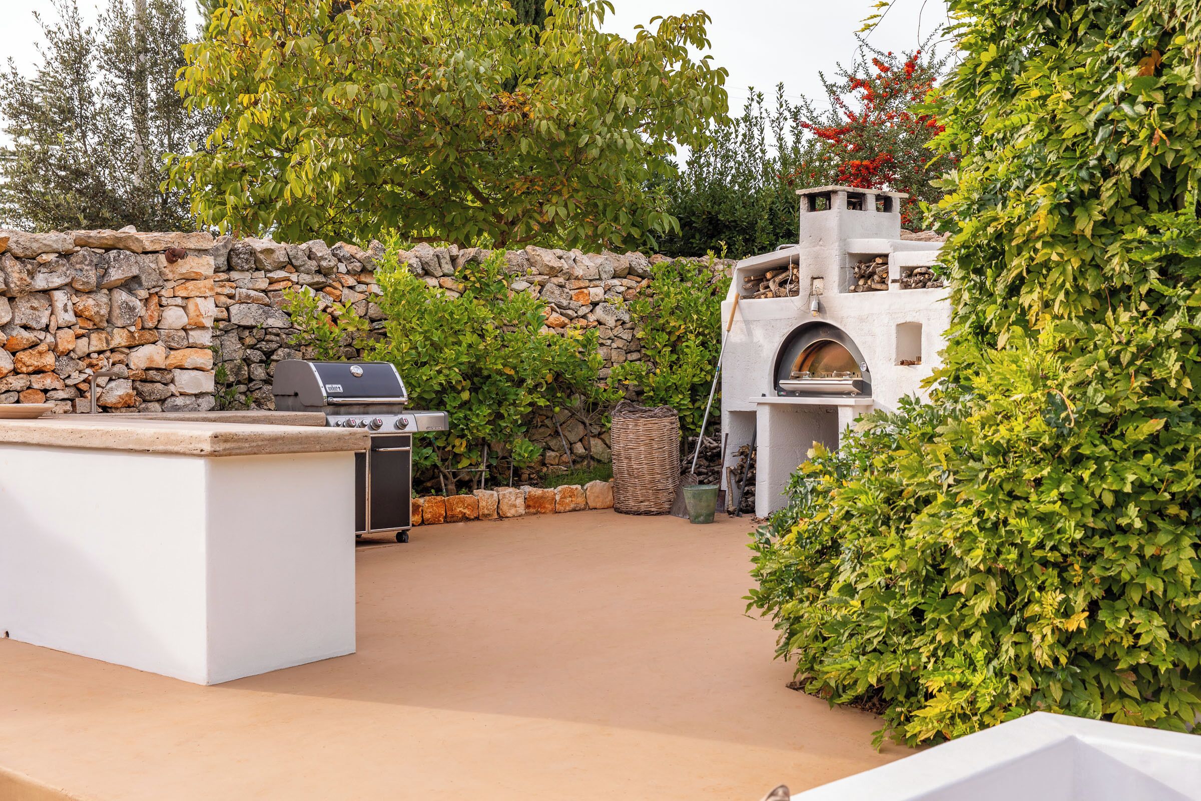 An outdoor patio with a stone wall, a grill, and a pizza oven.