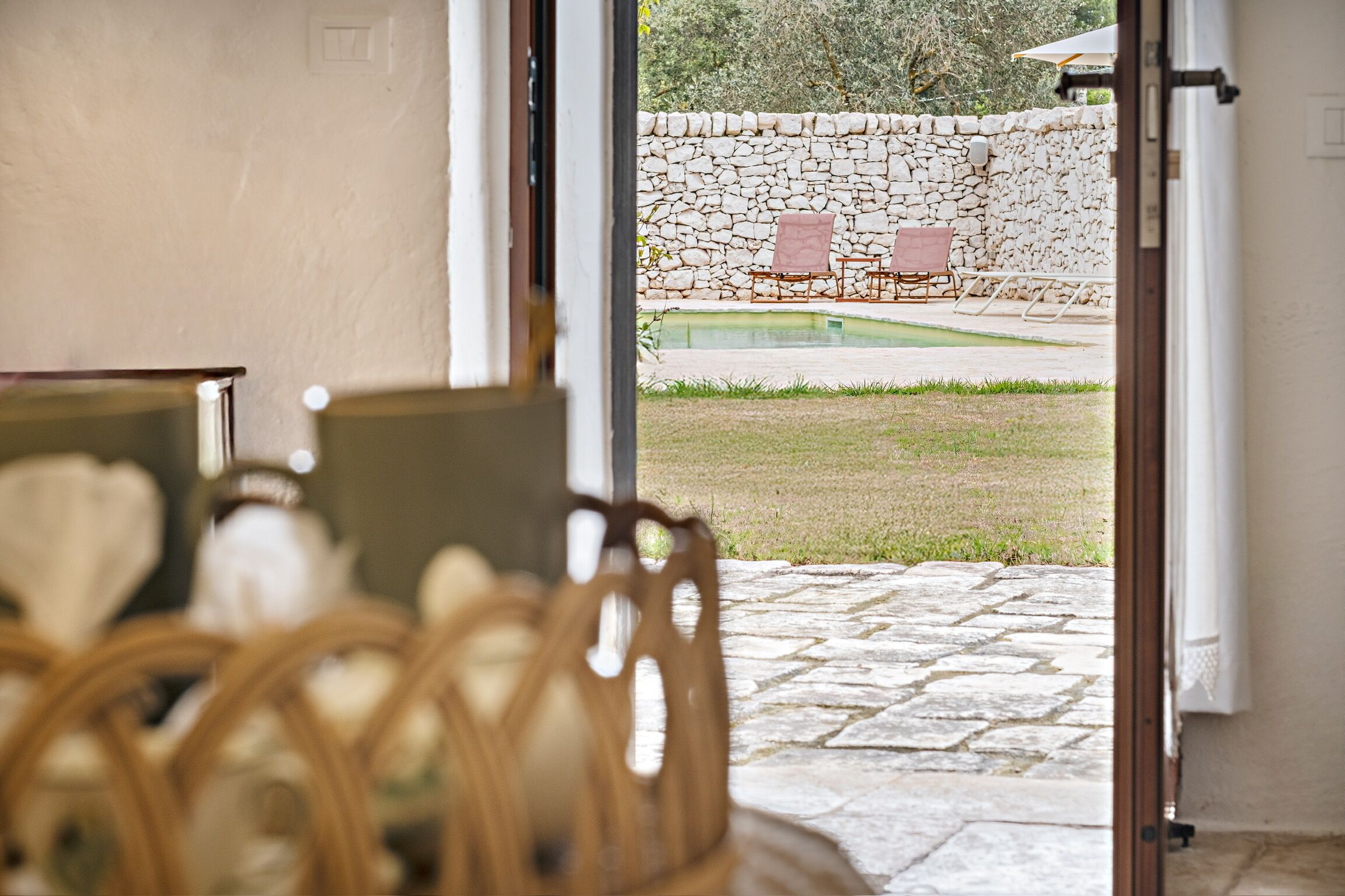 An open doorway to a stone-walled outdoor area with a pool, lounge chairs, and a stone pathway.