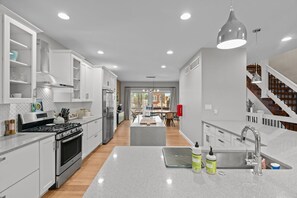Una cocina moderna con armarios blancos, una isla central, electrodomésticos de acero inoxidable y vistas al área de comedor.