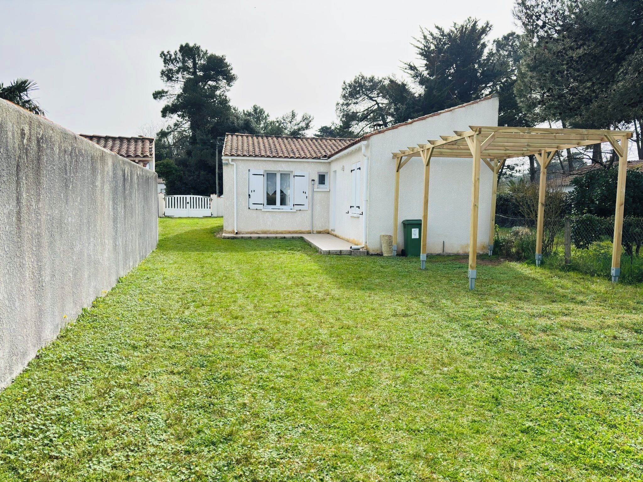 Ein kleines Haus mit Ziegeldach, einer Holzpergola und einem Rasen.