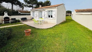 Ein kleines Haus mit Terrasse, Grill und Tisch mit Stühlen.