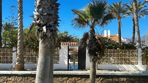 A courtyard with palm trees, a stone wall, and a white building with a tiled roof. - La Caleta 'Mediterranean beachfront house' (Caleta de Vélez)