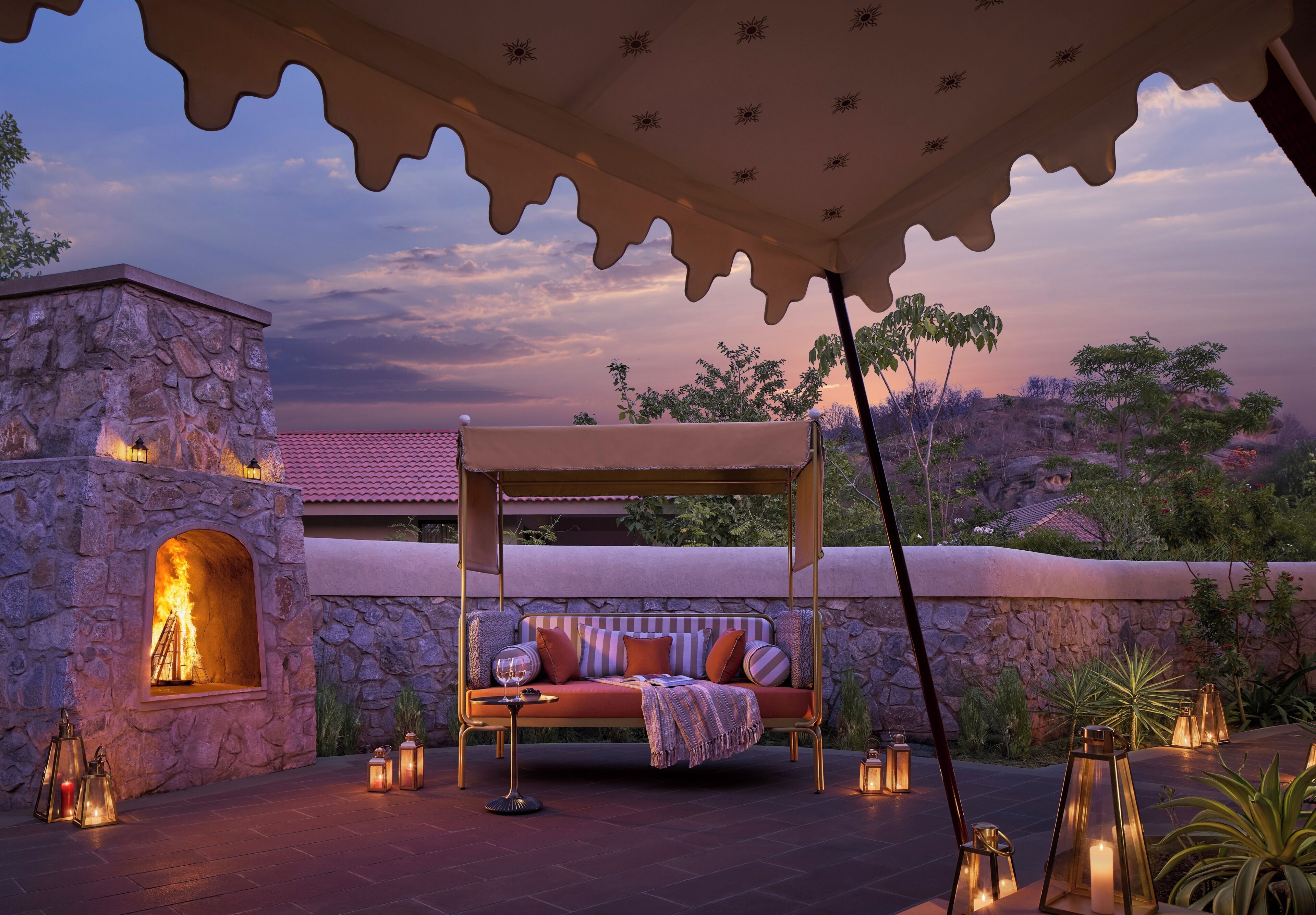 A stone building with a fire feature, a covered seating area with cushions, and lanterns.