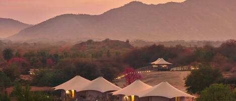 A series of dome-shaped tents with attached structures, set in a hilly landscape with trees and a mountain in the background.