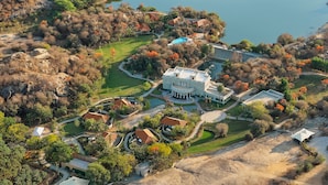 An aerial view of a large estate with multiple buildings, a swimming pool, and a lake. - Storii By ITC Hotels Jawai (Bali)