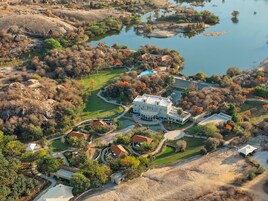 An aerial view of a large estate with multiple buildings, a swimming pool, and a lake.
