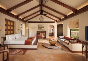 A spacious room with a large bed, a seating area, a dining table, and a view of the outdoors.