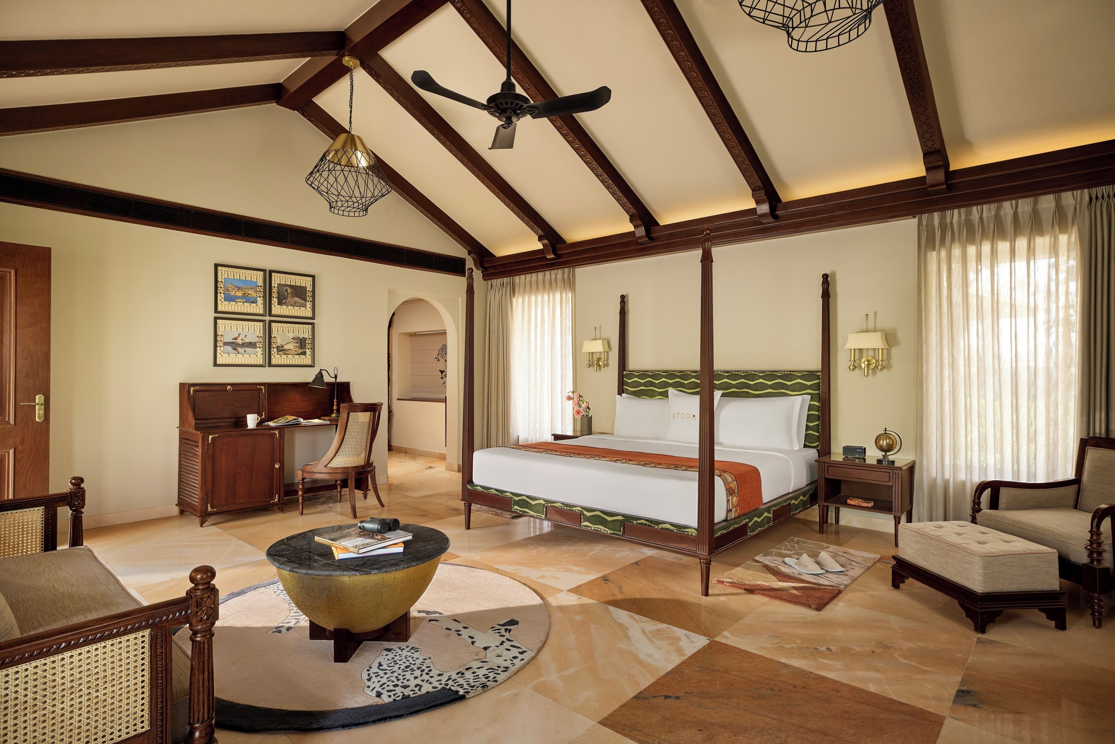 A spacious room with a large bed, a desk, a chair, and a round coffee table.