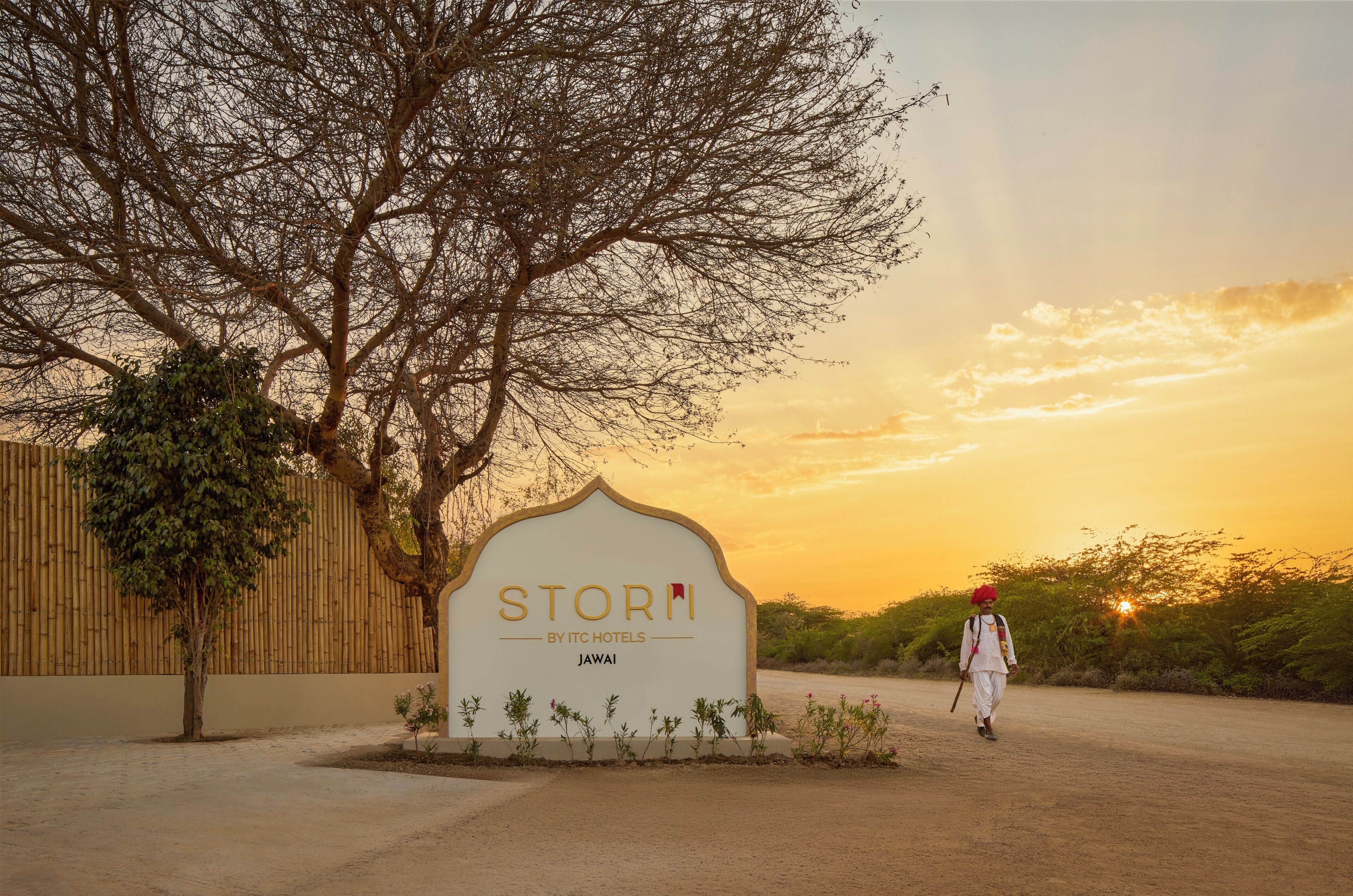 Een bord met de tekst 'STORM BY ITC HOTELS JAWA', met een boom en een persoon op de achtergrond.