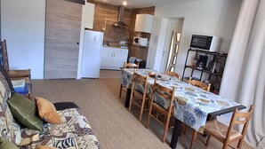 Een woonkamer met een bank, een eettafel met stoelen, een keuken met apparatuur en een schuifdeur.