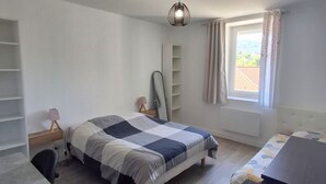 Een slaapkamer met een bed, nachtkastjes, een bureau, een stoel, een kledingkast en een raam met gordijnen.