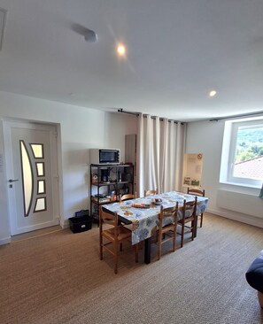 A dining area with a table set for four, a microwave on a shelf, and a window with a view of greenery. - Country getaway (Charavines)