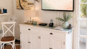 A room with a white cabinet, a chair, a fan, a vase with stones, and a wall-mounted TV displaying a phone number and website.