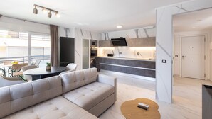 A modern living room with a sofa, a dining table, and a kitchen area with a TV. - AURA Superior Apartment (La Pineda)