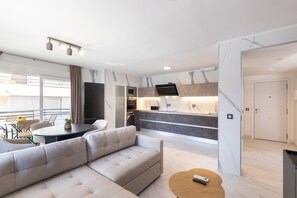 Ein modernes Wohnzimmer mit einer Couch, einem Esstisch und einer Küchenzeile mit Fernseher.