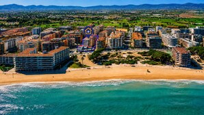 An aerial view of a coastal city with a beachfront, high-rise buildings, and a prominent hotel icon. - AURA Superior Apartment (La Pineda)