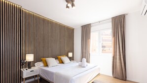 A modern hotel room with a bed, bedside tables, a lamp, and a window with curtains. - AURA Superior Apartment (La Pineda)