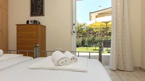 A hotel room with two beds, a wooden dresser, a painting on the wall, and a view of a garden and building outside.