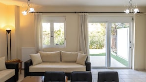 A living room with a sofa, two armchairs, a coffee table, a chandelier, and a view through a sliding glass door.