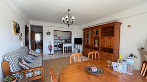 Una sala de estar con sofá, mesa de comedor, sillas, candelabro, cocina al fondo y chimenea.