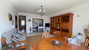 Una sala de estar con sofá, mesa de comedor, sillas, candelabro, cocina al fondo y chimenea.