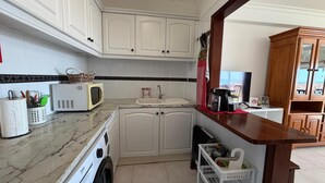 Una cocina con armarios blancos, un microondas, un fregadero y una mesa de madera.