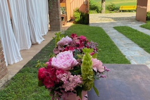 Un jardin avec un arrangement floral sur une table, un mur de briques et un banc jaune en arrière-plan.