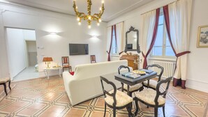 Una sala de estar con un sofá blanco, una mesa de comedor con sillas, una araña, un televisor y un piso estampado.