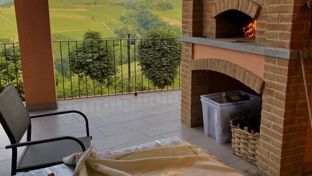 Un balcón con un horno de ladrillo, una silla y vistas a colinas ondulantes.
