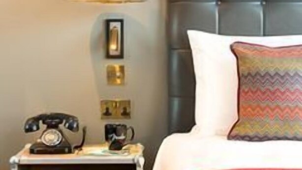 A neatly arranged bedroom with a bed, bedside table, lamp, and wall-mounted speakers. - Hotel Indigo Cardiff (Cardiff)