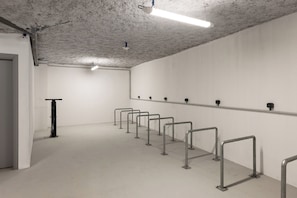 Un espace intérieur propre et moderne, avec une rangée de rampes métalliques le long du mur, une porte sur la gauche et un plafond où les tuyaux et les luminaires sont apparents.
