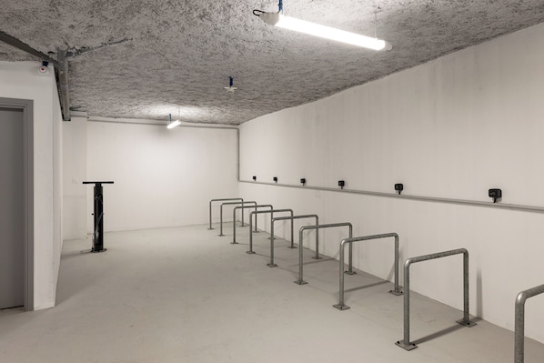 Un espacio interior limpio y moderno con una fila de barandales metálicos a lo largo de la pared, una puerta a la izquierda y un techo con tuberías y luminarias expuestas.