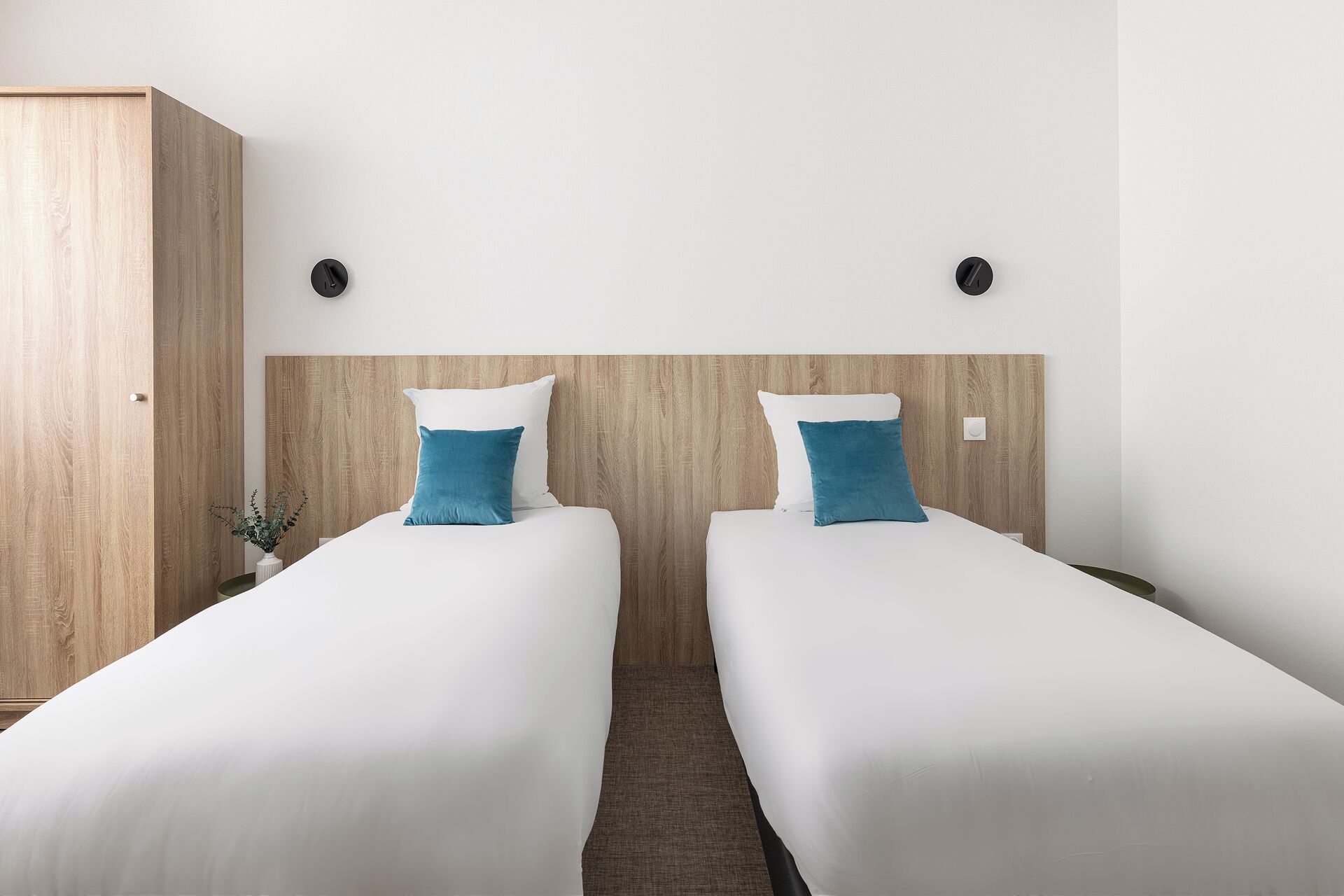 A hotel room with two single beds, a wooden wardrobe, and a small potted plant.