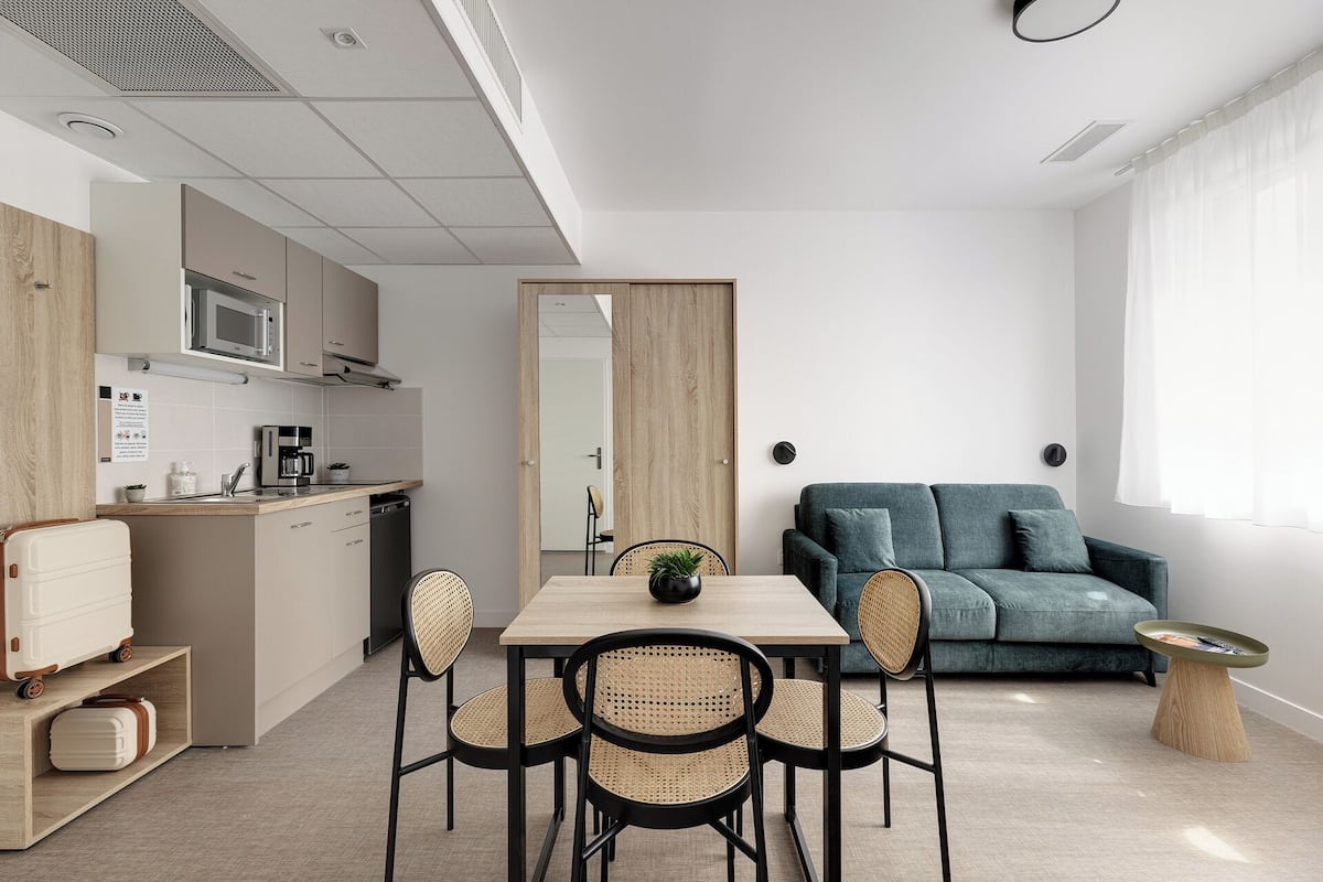 Um apartamento moderno com cozinha compacta, área de refeições com mesa e cadeiras, sofá e uma pequena mesinha lateral.