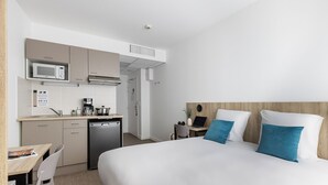Hotellihuone, jossa on sänky, työpöytä tuolilla, pieni keittiö mikroaaltouunilla sekä kahvinkeitin.
