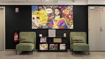 A lobby with two green armchairs, a fire extinguisher, a checkered board, and a Monopoly game.
