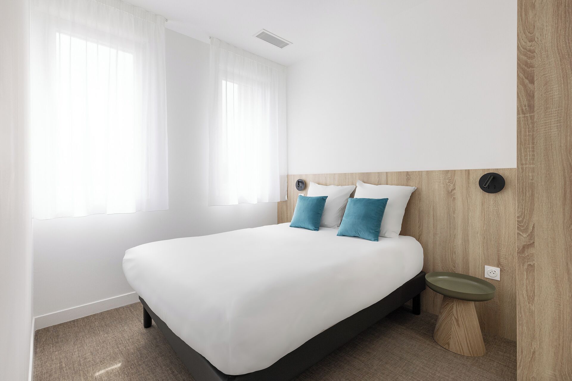 Habitación de hotel moderna con una cama grande, una mesita de noche y una lámpara fijada a la pared.