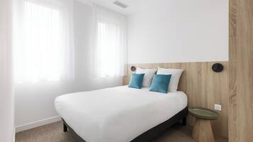 Habitación de hotel moderna con una cama grande, una mesita de noche y una lámpara fijada a la pared.
