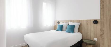Habitación de hotel moderna con una cama grande, una mesita de noche y una lámpara fijada a la pared.