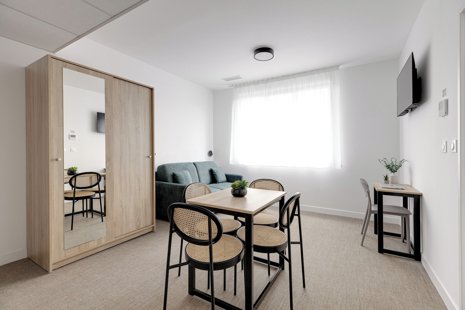 Una habitación moderna con una mesa de comedor, sillas, un sofá y un televisor montado en la pared.