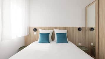 Ein Hotelzimmer mit Bett, zwei Kissen, einem Nachttisch, einem Spiegel und einem Holz-Kopfteil.