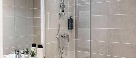 A modern bathroom with a glass shower enclosure, a white sink with a wooden cabinet, and a mirror.