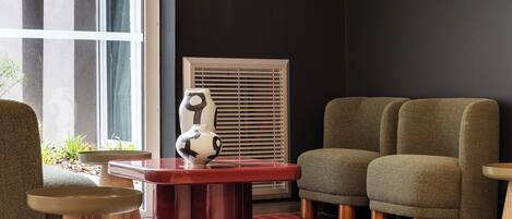 A modern living room with a red coffee table, two green armchairs, a white vase, and a large window.