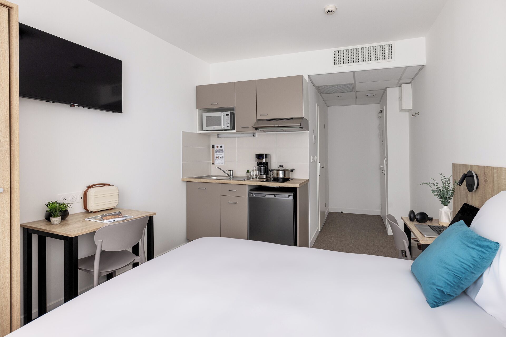 Una habitación de hotel compacta con kitchenette, cama, escritorio y televisión.